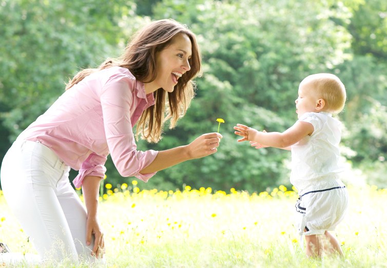 Happy mother teaching baby to walk in the park