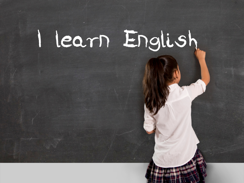 schoolgirl writing I learn English with chalk on blackboard school classroom