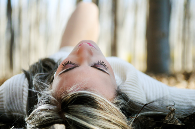 Beautiful blonde girl lying on leaves in a forest of poplars