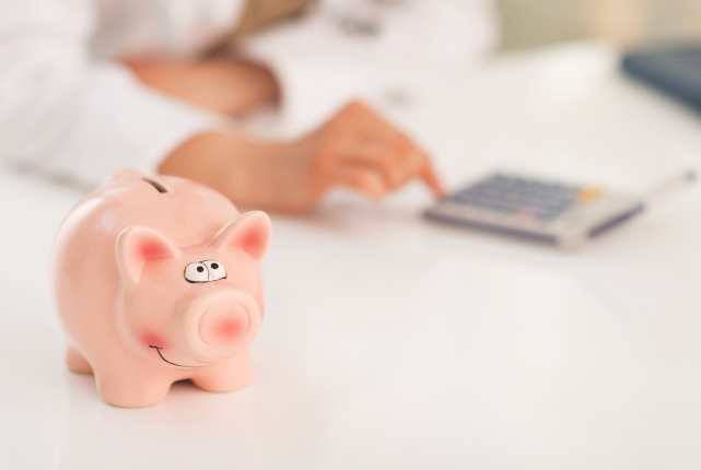 Closeup on piggy bank and medical doctor woman using calculator in background