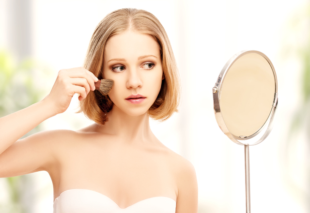 beautiful woman doing  makeup with brush in the mirror