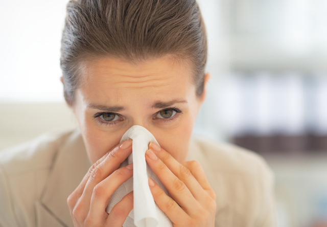 Portrait of business woman in office blowing nose