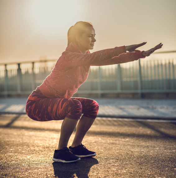 Athletic woman doing squats on a road at sunset.