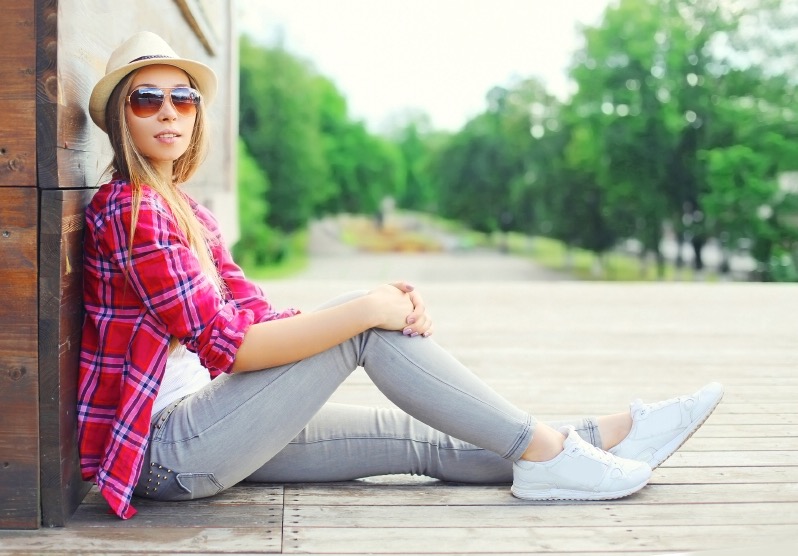 pretty young woman wearing a pink shirt and summer hat sitting resting in city over green park