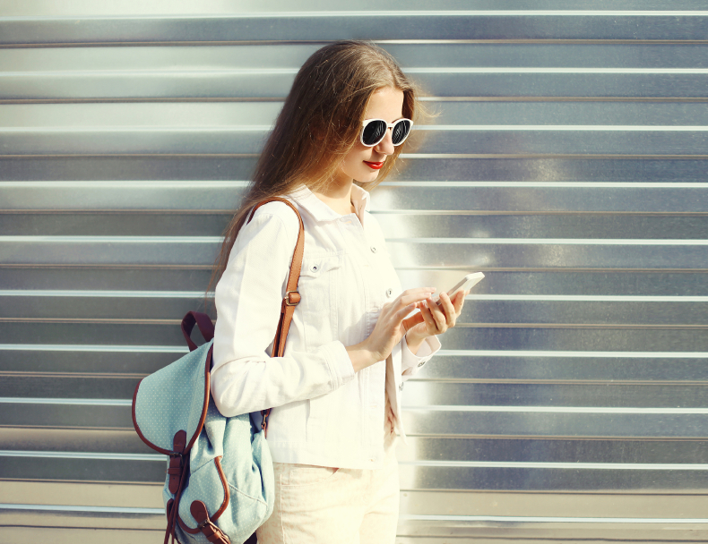 Fashion pretty young woman using smartphone in city over urban g