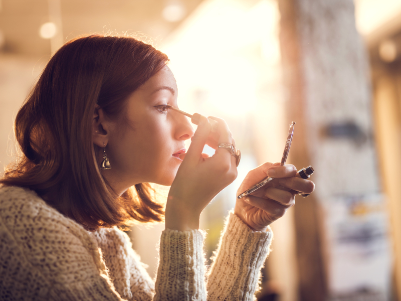 Woman holding hand mirror and fixing make-up.