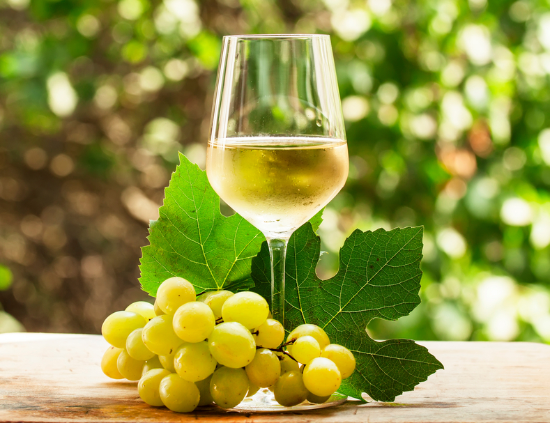 Coid white wine and green grapes on natural blurred background